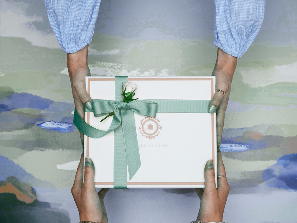 Un coffret cadeau noué d’un ruban vert, tendu à deux mains